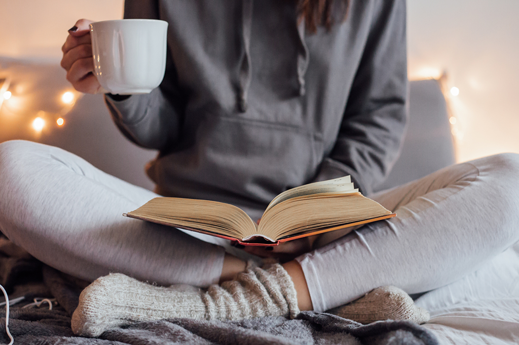 Pessoa a ler um livro enquanto toma um chá ou outra bebida reconfortante.