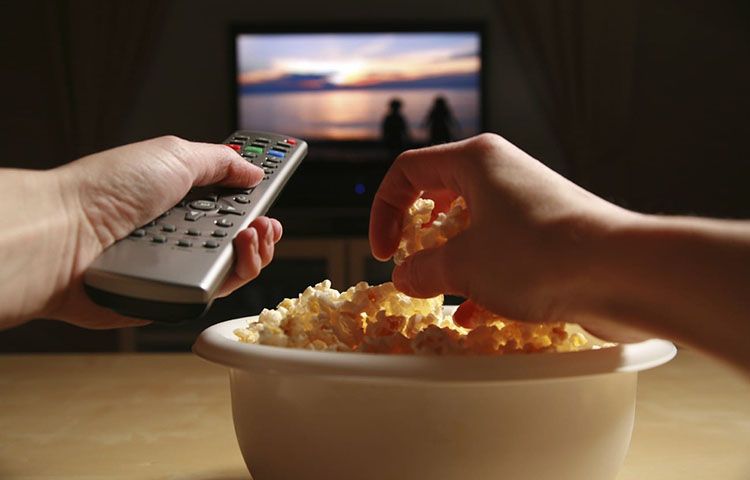 Pessoa a ver um filme ou série enquanto come pipocas.